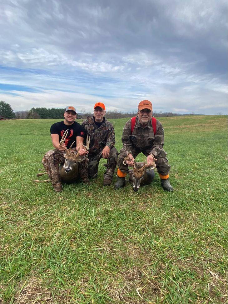 Three hunters kneeling behind two whitetail bucks in a green field